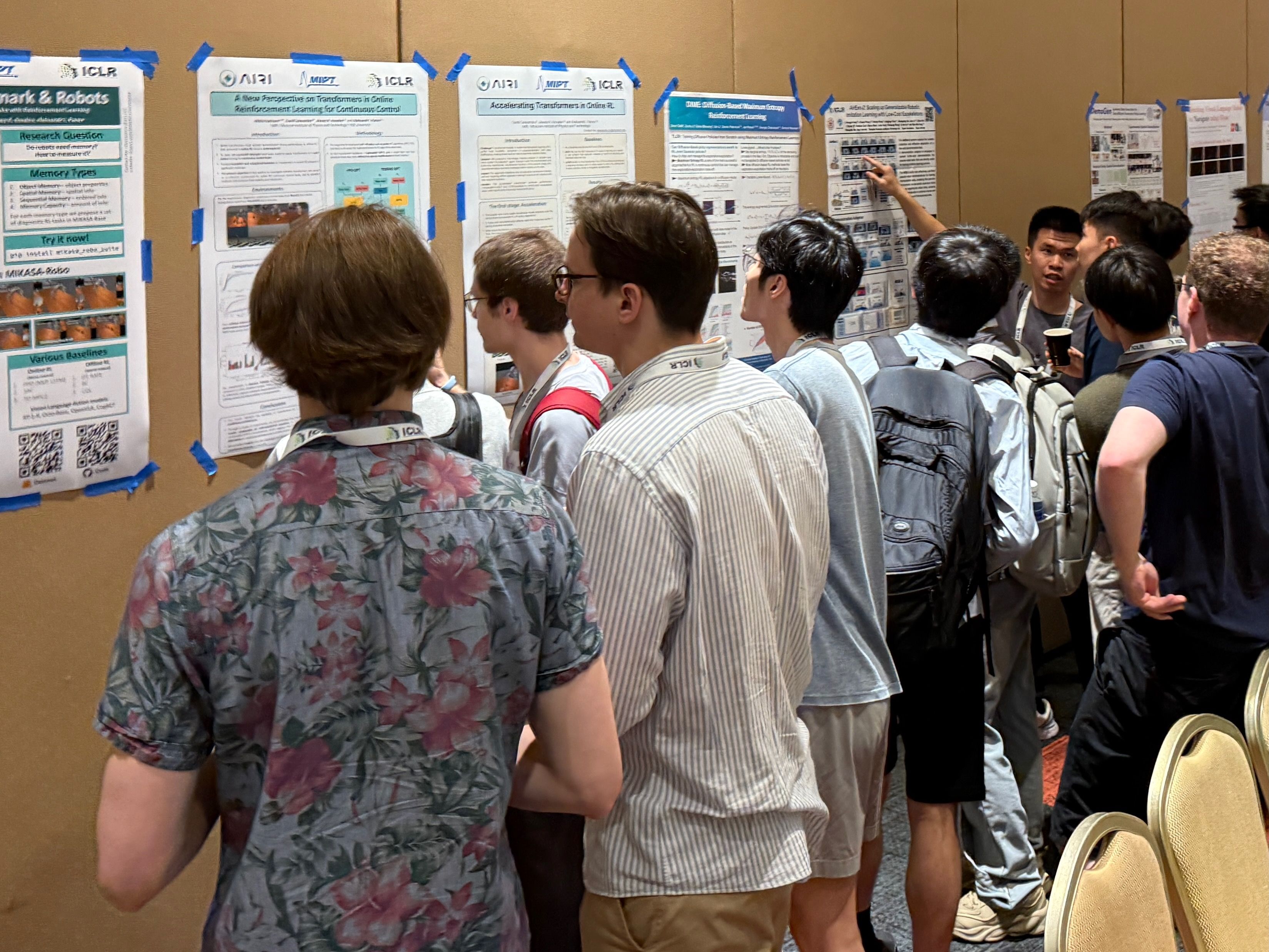 Researchers gather around posters stuck to the wall of the room. Some are engaged in conversation. 